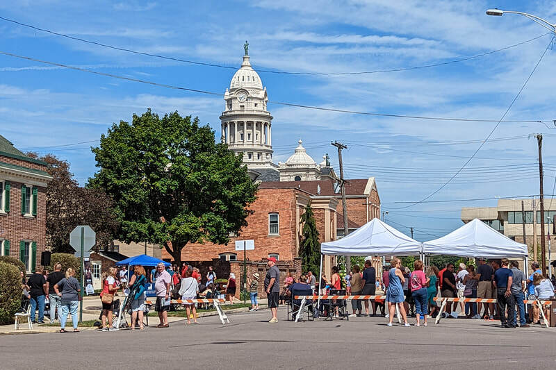 A scenic landscape of Troy Ohio's artisan tent village with the courthouse in the background and a blue cloudy sky