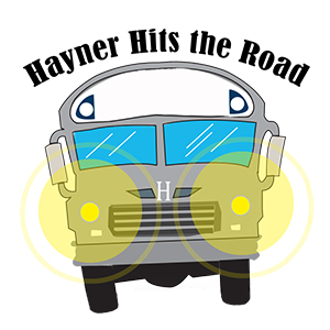 A grey bus from the front with bright yellow headlights and the words 'Hayner Hits the Road' above it